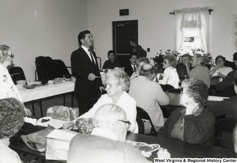 Representative Nick J. Rahall (D-W.Va.) stands and gives a speech at a event attended by older people.